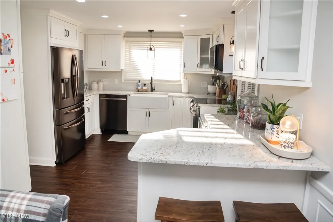 Kitchen featuring light stone countertops, white cabinets, stainless steel appliances, dark LVT finished floors, and a kitchen bar
