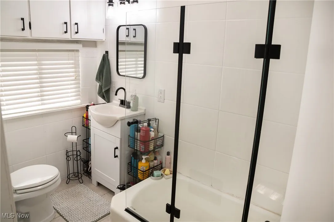 Full bath featuring vanity, a tub with shower, and tile walls