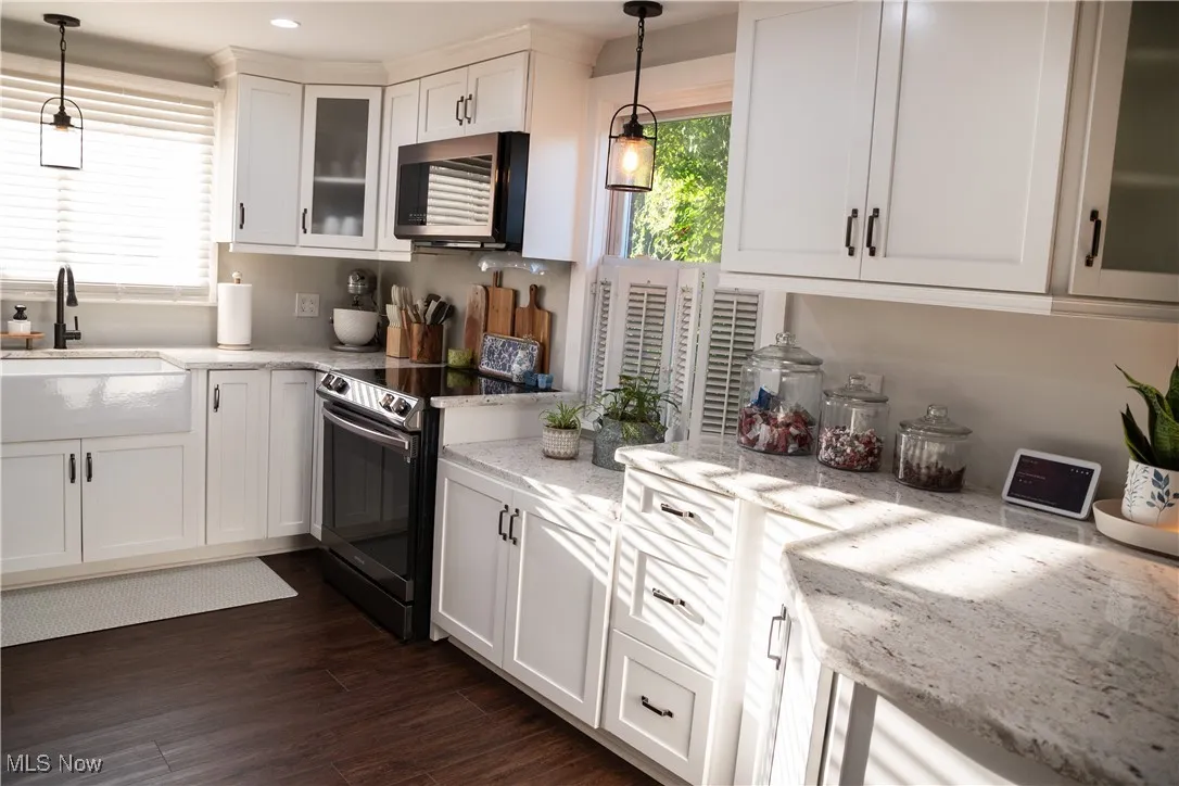 Kitchen with glass insert cabinets, hanging light fixtures, light stone countertops, white cabinets, and recessed lighting