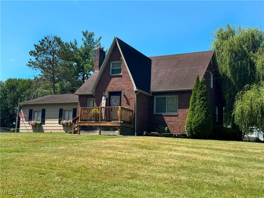 View of front of home featuring brick siding, a front lawn, a chimney, and a deck