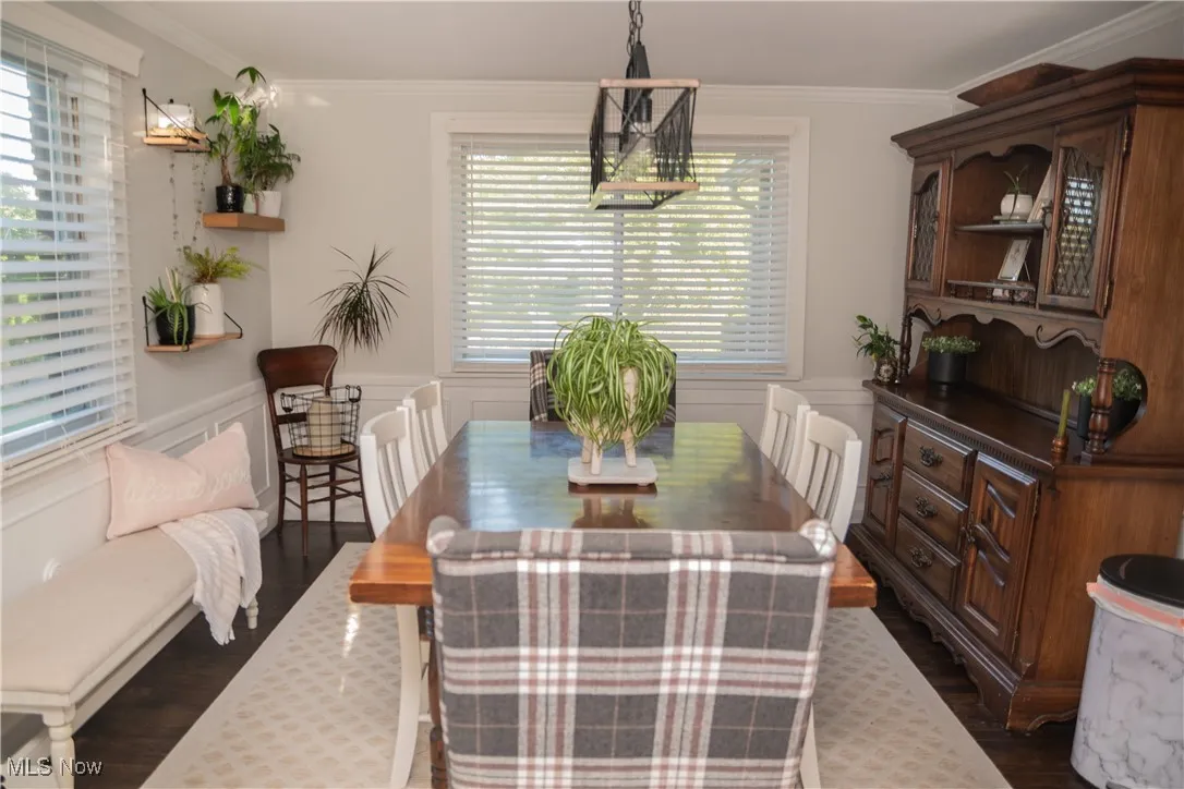 Dining room with crown molding, dark wood-style flooring, wainscoting, and a decorative wall