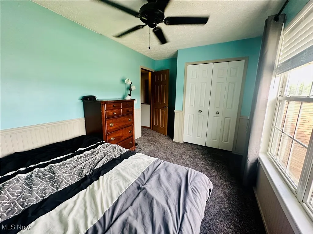 Carpeted bedroom featuring a textured ceiling, ceiling fan, a closet, and a wainscoted wall