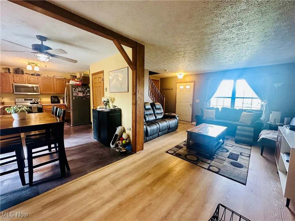 Living area featuring dark wood-type flooring, a textured ceiling, stairs, and a ceiling fan