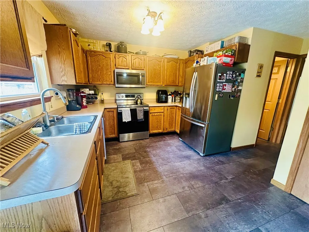 Kitchen with stainless steel appliances, light countertops, brown cabinets, a textured ceiling, and dark stone finish floors