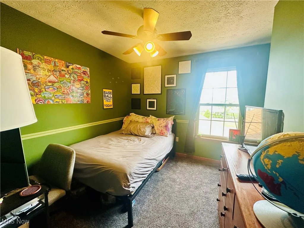 Bedroom with a textured ceiling, carpet flooring, and ceiling fan