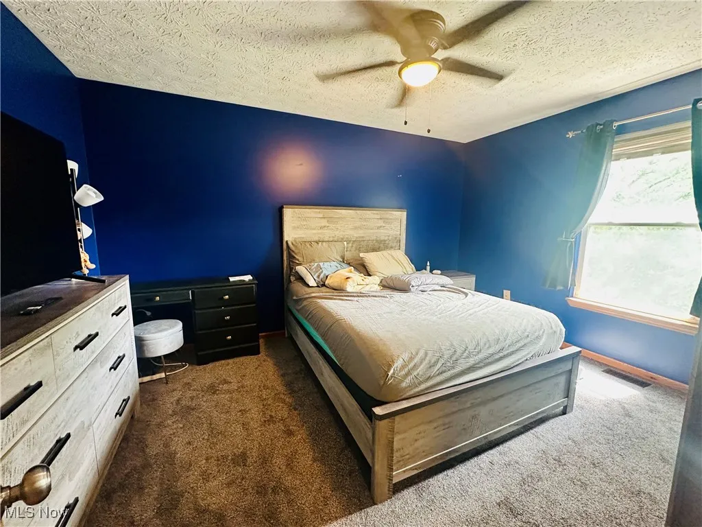 Bedroom with dark colored carpet, ceiling fan, and a textured ceiling