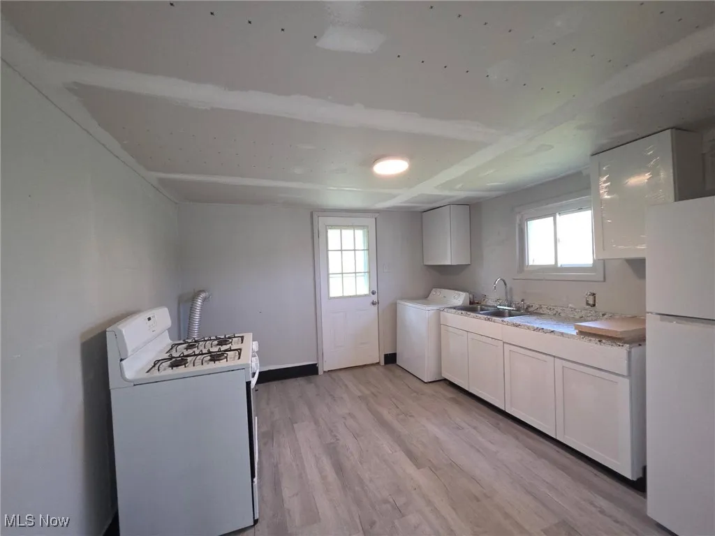 Kitchen featuring white appliances, light wood finished floors, washer / clothes dryer, light countertops, and white cabinetry