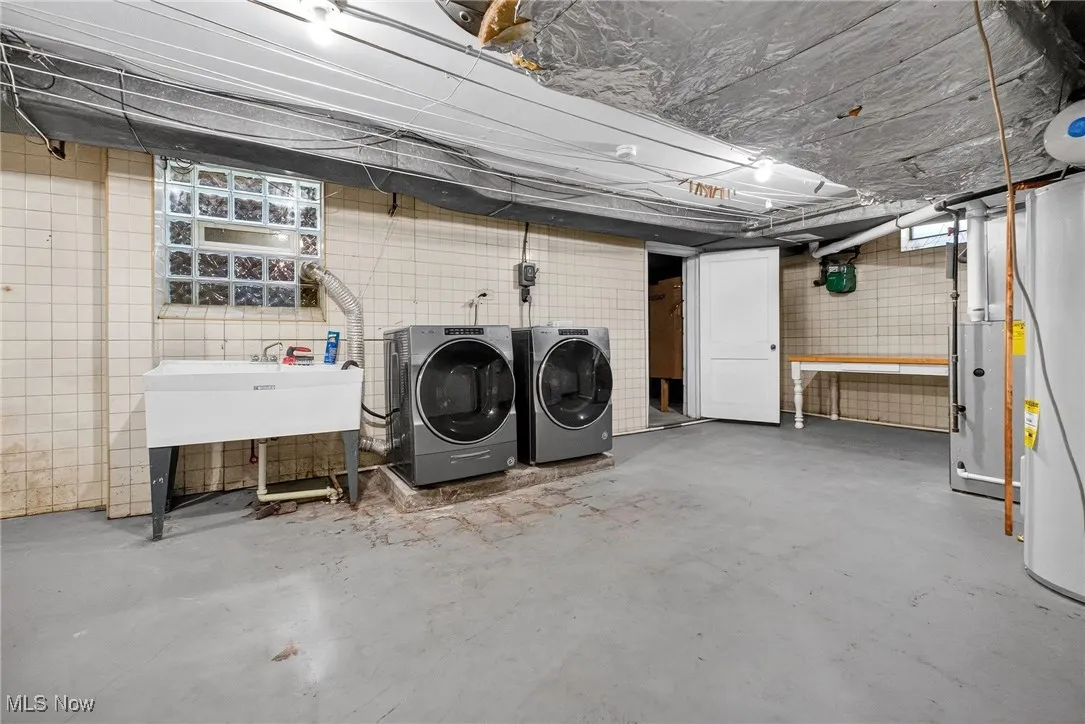 Unfinished basement with washer and dryer, water heater, and heating unit