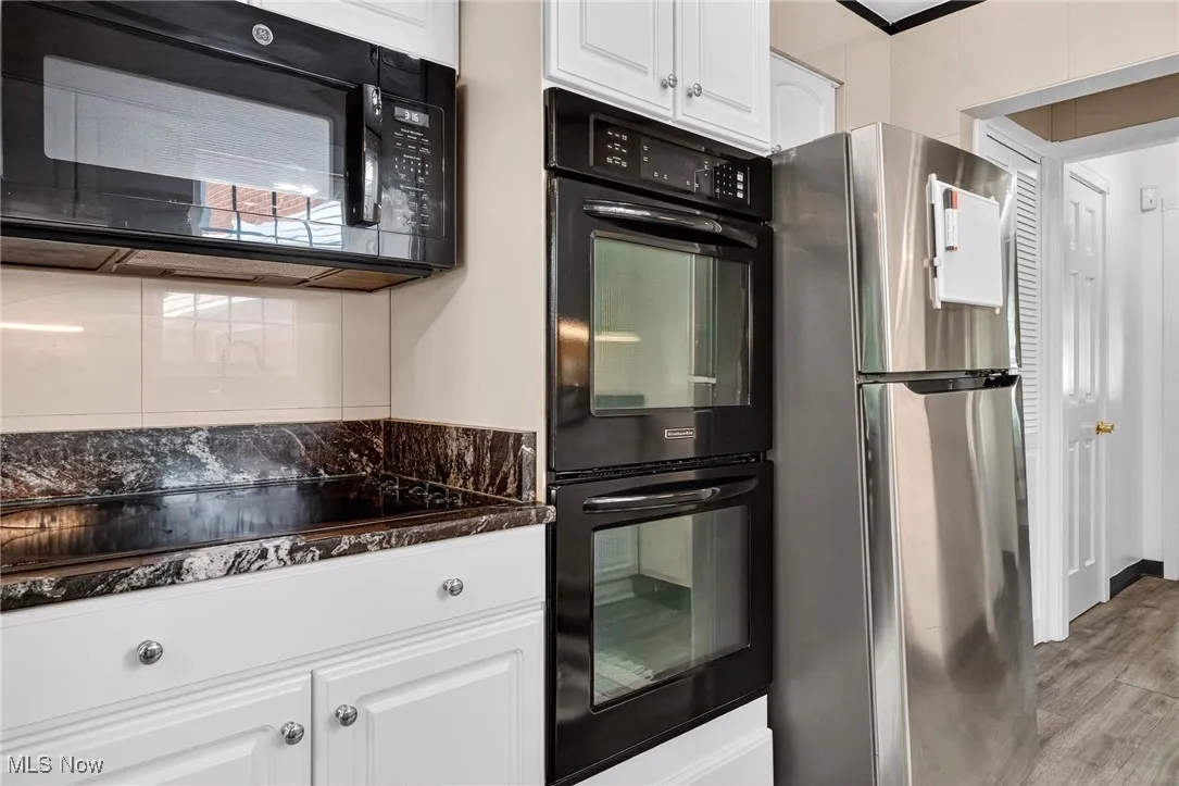 Kitchen with white cabinetry, black appliances, light wood-style flooring, and dark stone countertops