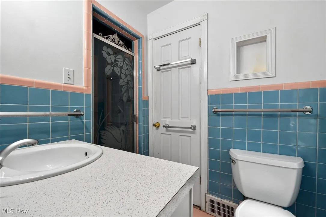 Full bath featuring vanity, tile walls, wainscoting, and a shower stall