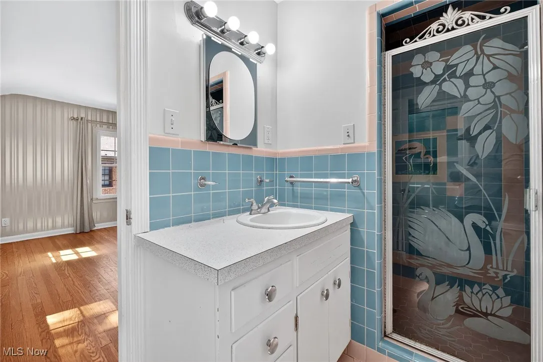 Bathroom featuring a shower stall, vanity, tile walls, light wood-style floors, and a wainscoted wall