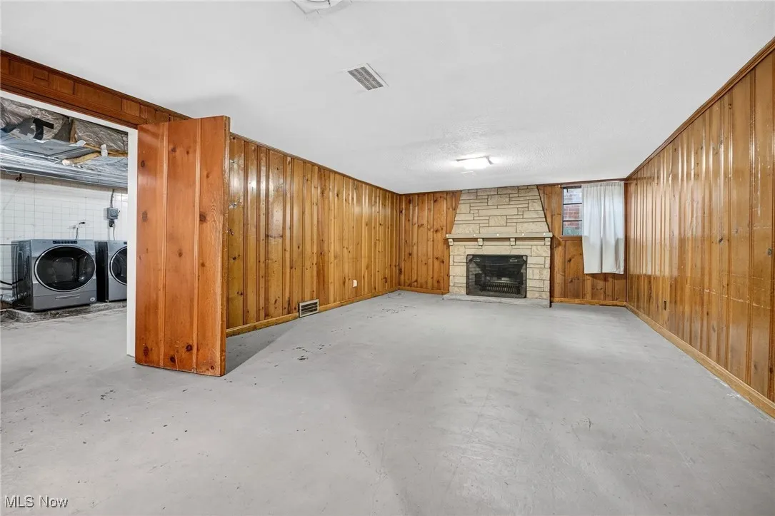 Unfurnished living room with wood walls, a stone fireplace, concrete floors, and independent washer and dryer