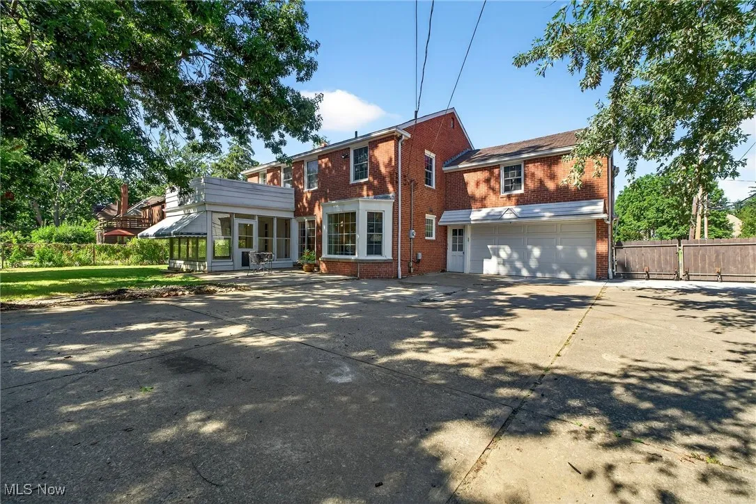 View of front facade with brick siding, a sunroom, driveway, and an attached garage
