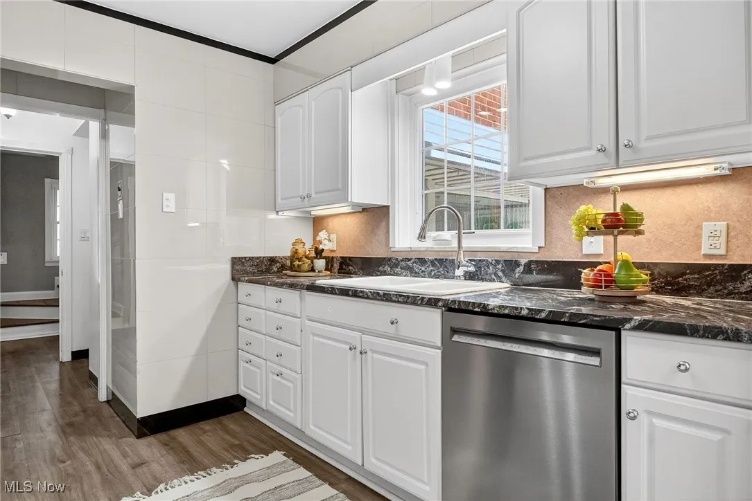 Kitchen with dishwasher, white cabinetry, dark stone countertops, and dark wood-type flooring