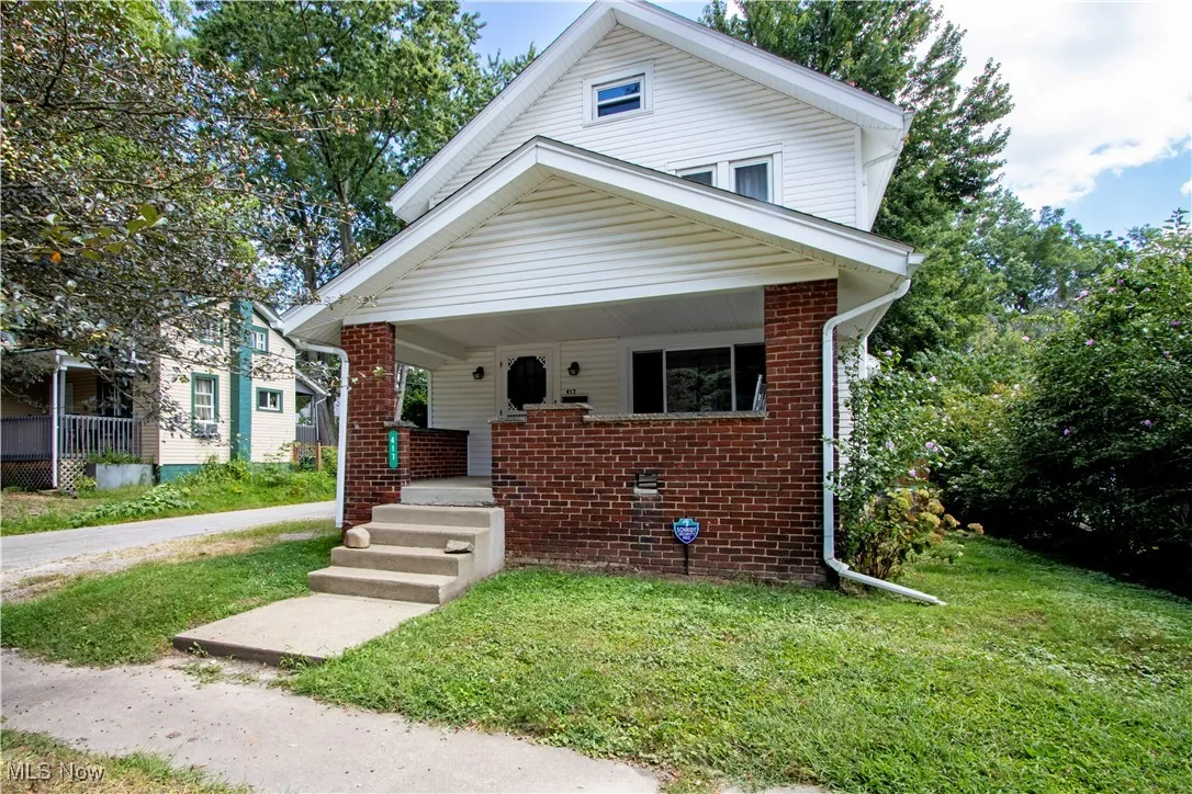 Bungalow-style house featuring covered porch, brick siding, and a front lawn