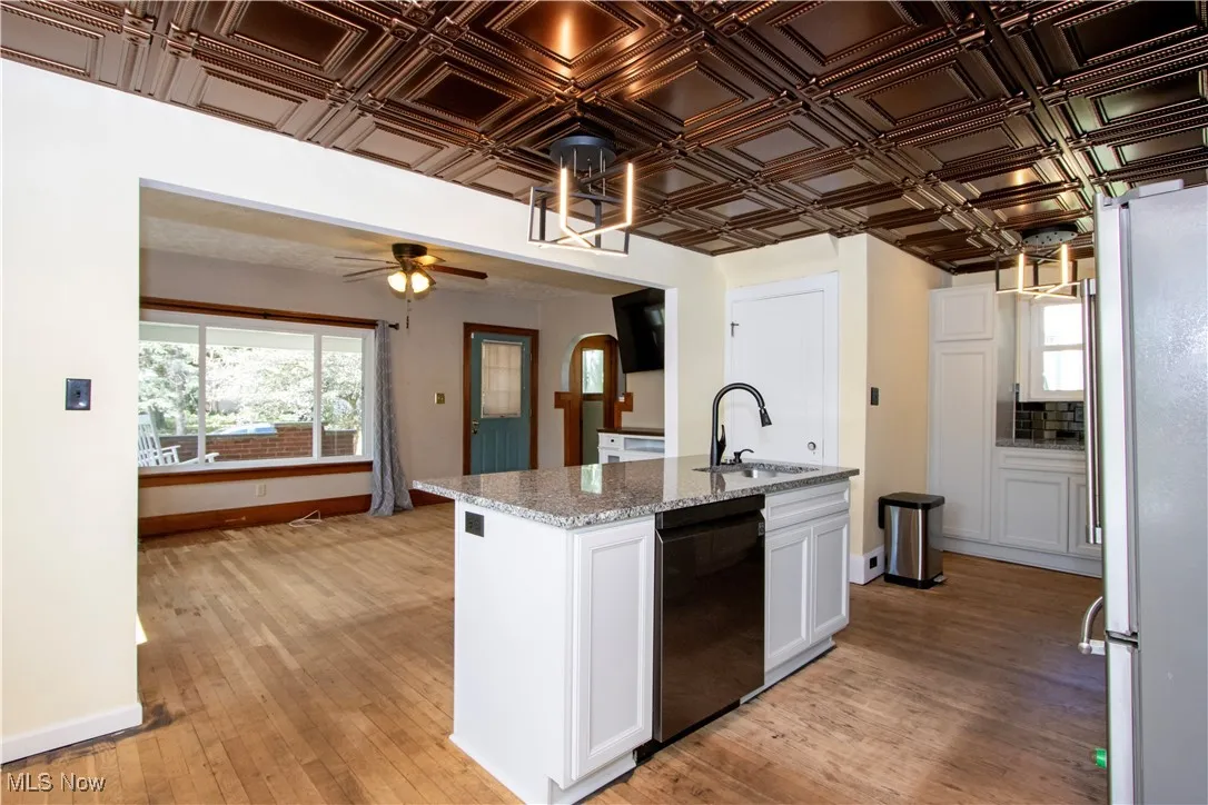 Kitchen with freestanding refrigerator, light stone counters, white cabinetry, light wood finished floors, and black dishwasher