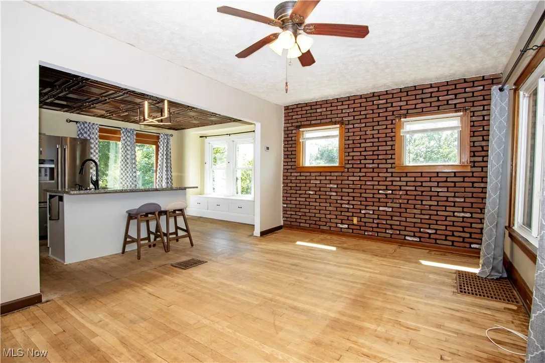 Living area featuring brick wall, healthy amount of natural light, light wood-type flooring, and a ceiling fan