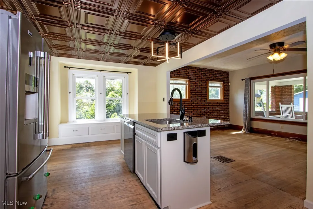 Kitchen with stainless steel appliances, dark stone counters, a kitchen island with sink, white cabinetry, and light wood-style floors