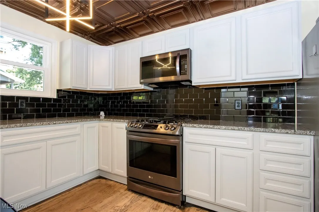 Kitchen with white cabinets, appliances with stainless steel finishes, tasteful backsplash, and an ornate ceiling