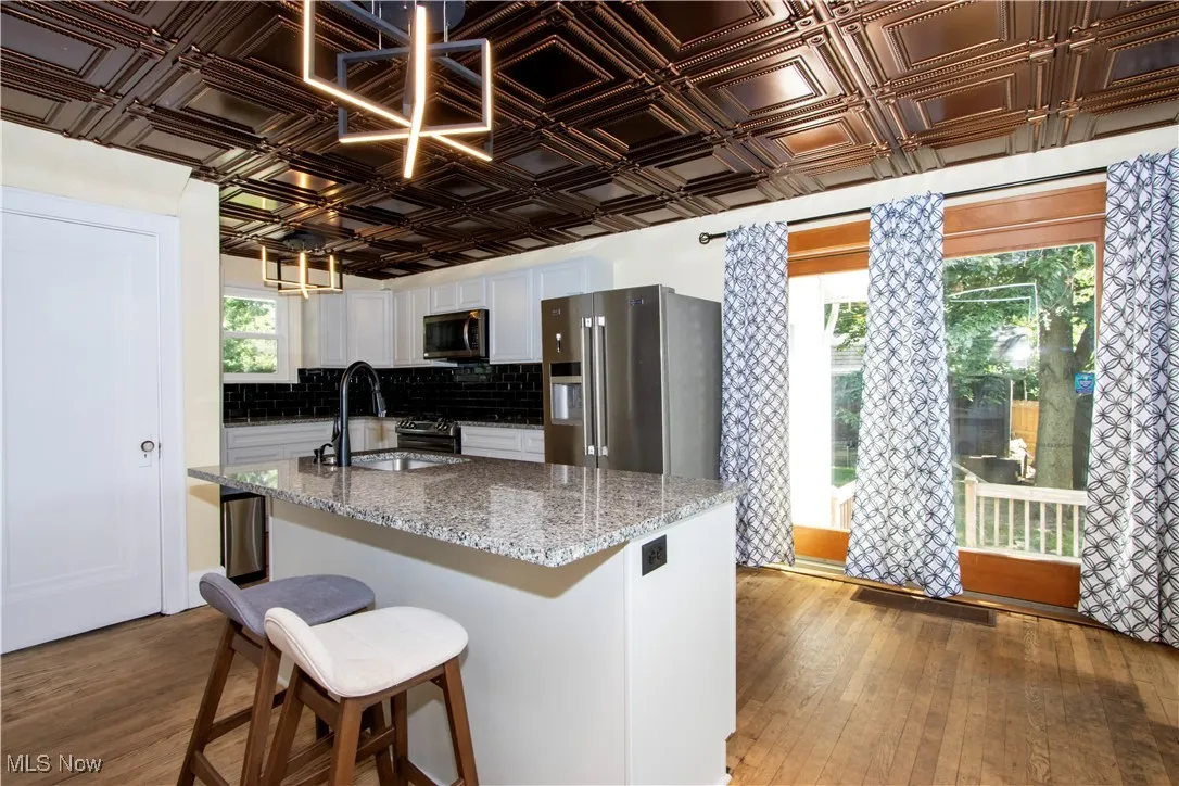 Kitchen with light stone countertops, dark wood-style floors, stainless steel appliances, a kitchen bar, and an ornate ceiling