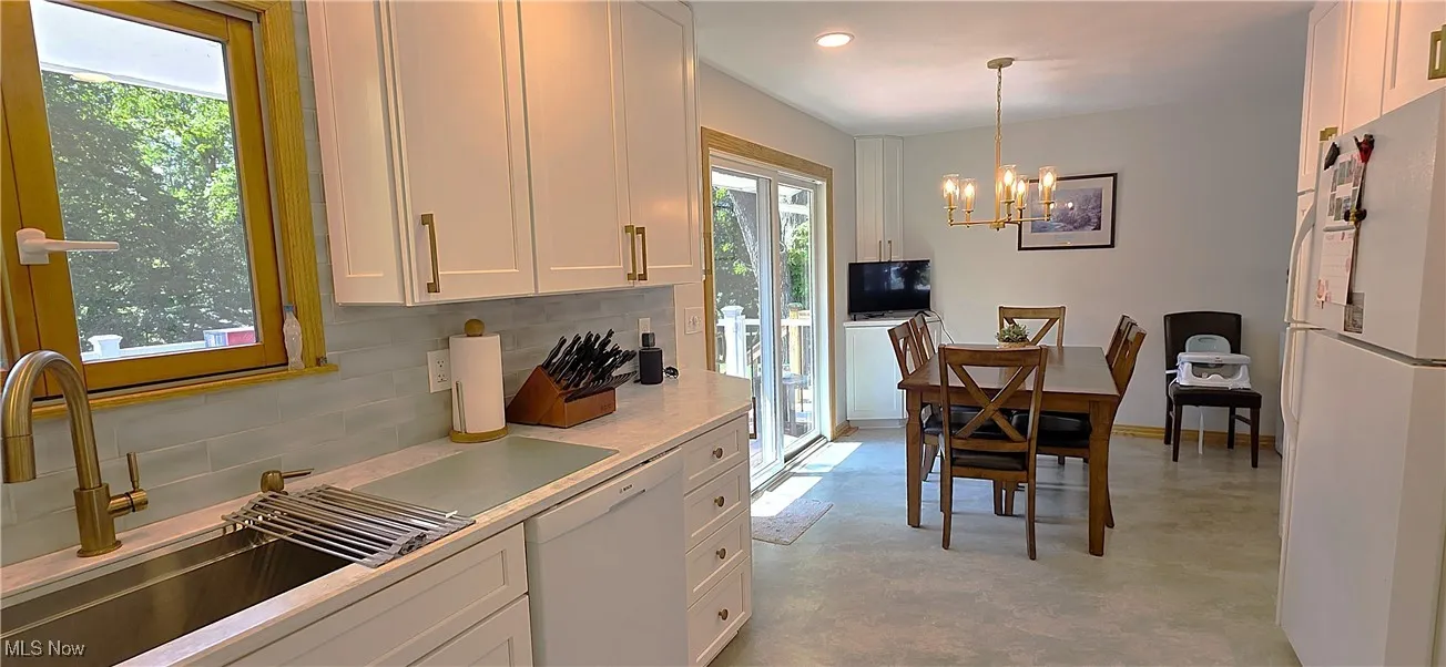 Kitchen with backsplash, white appliances, white cabinets, light countertops, and pendant lighting