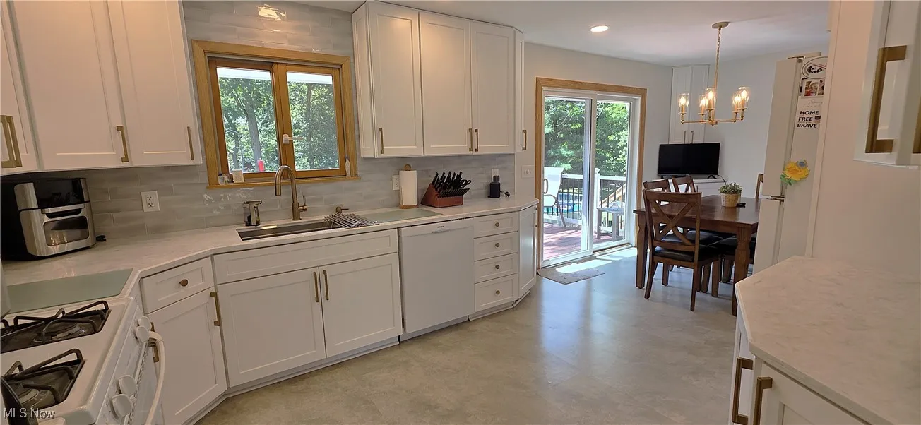 Kitchen with decorative backsplash, white cabinetry, white appliances, and a chandelier