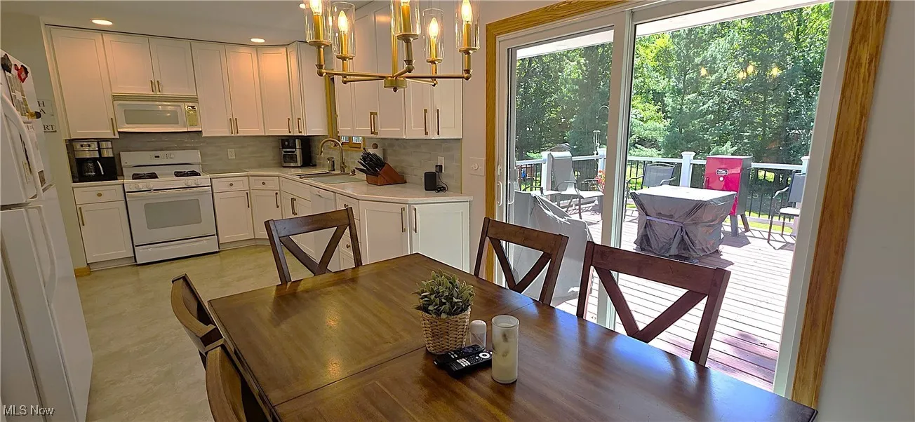 Kitchen with a chandelier, white appliances, pendant lighting, light countertops, and white cabinetry