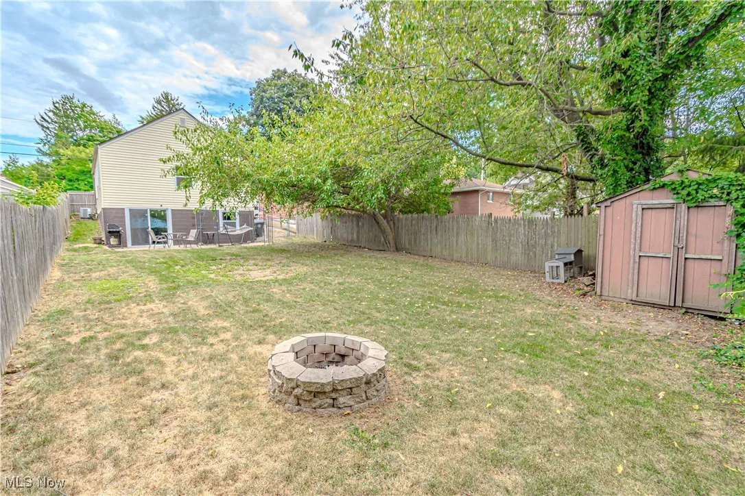 Fenced backyard featuring a fire pit, a patio area, and a storage unit