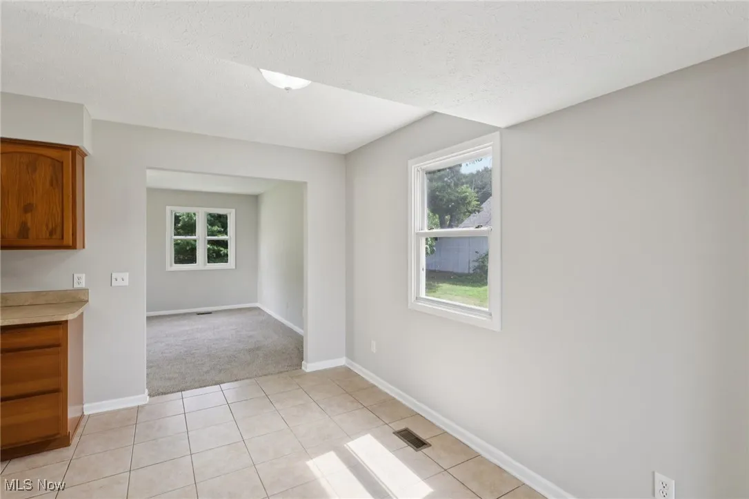 Unfurnished room featuring light tile patterned flooring, a textured ceiling, and light carpet