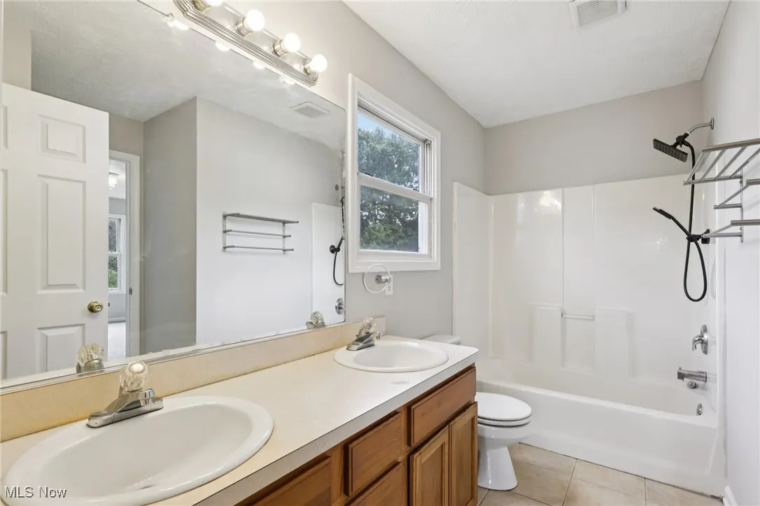 Bathroom featuring shower / bathtub combination, light tile patterned floors, and double vanity