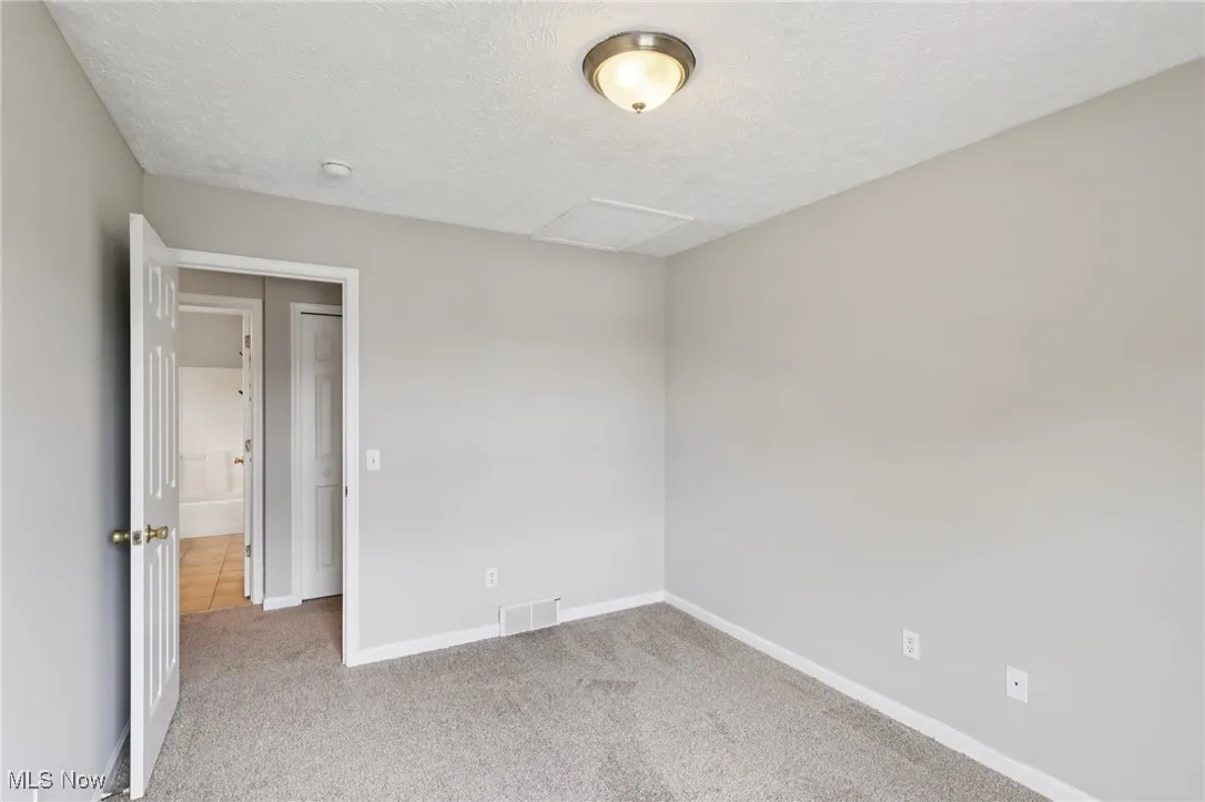 Empty room featuring light colored carpet, a textured ceiling, and attic access