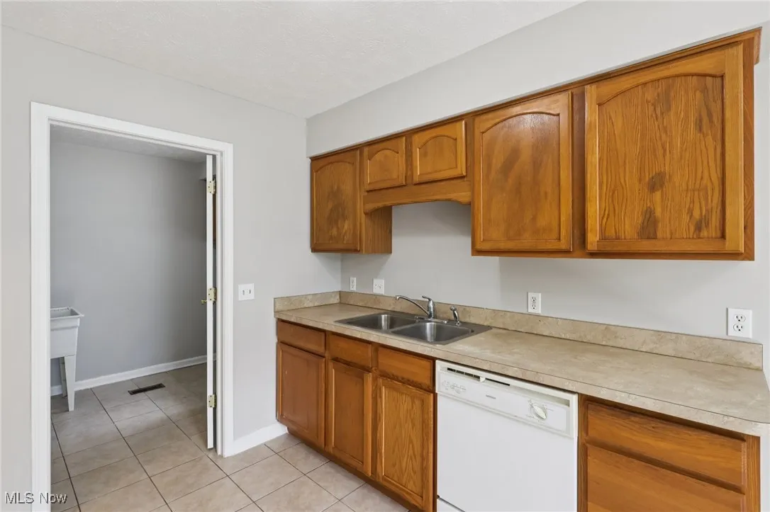 Kitchen with white dishwasher, brown cabinetry, light countertops, and light tile patterned floors