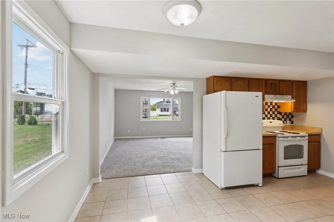 Kitchen with white appliances, light tile patterned floors, brown cabinetry, light countertops, and backsplash