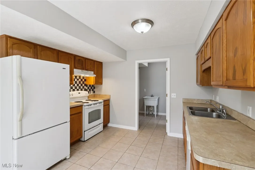 Kitchen with white appliances, light tile patterned floors, light countertops, backsplash, and under cabinet range hood