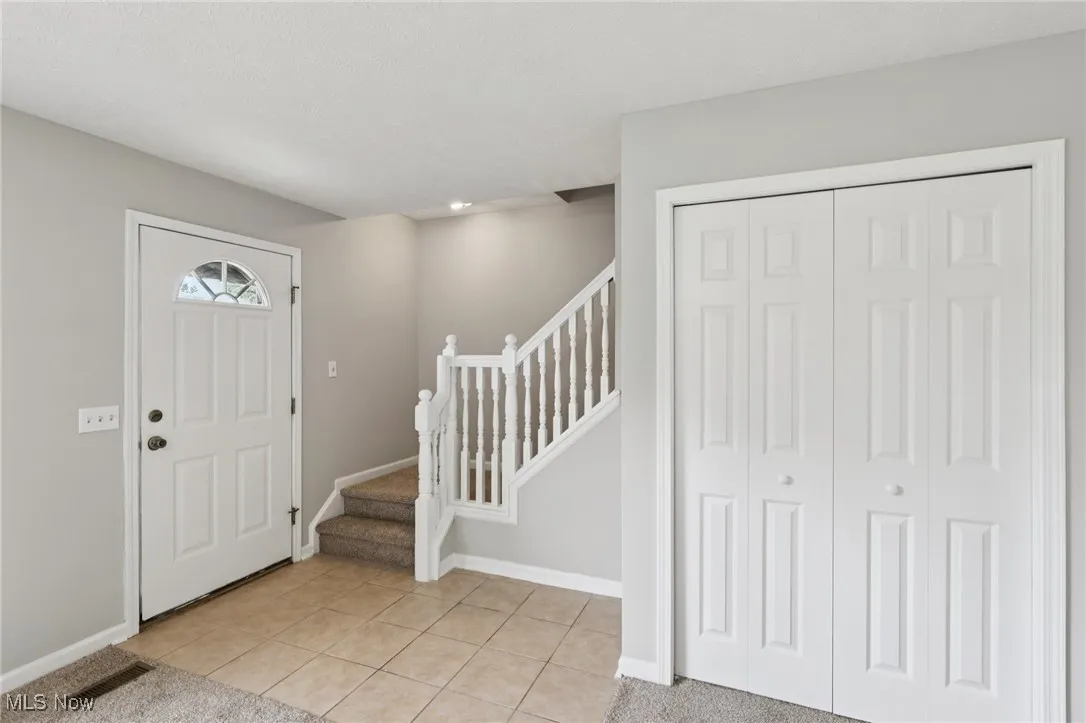 Foyer featuring stairway, light tile patterned flooring, and light colored carpet