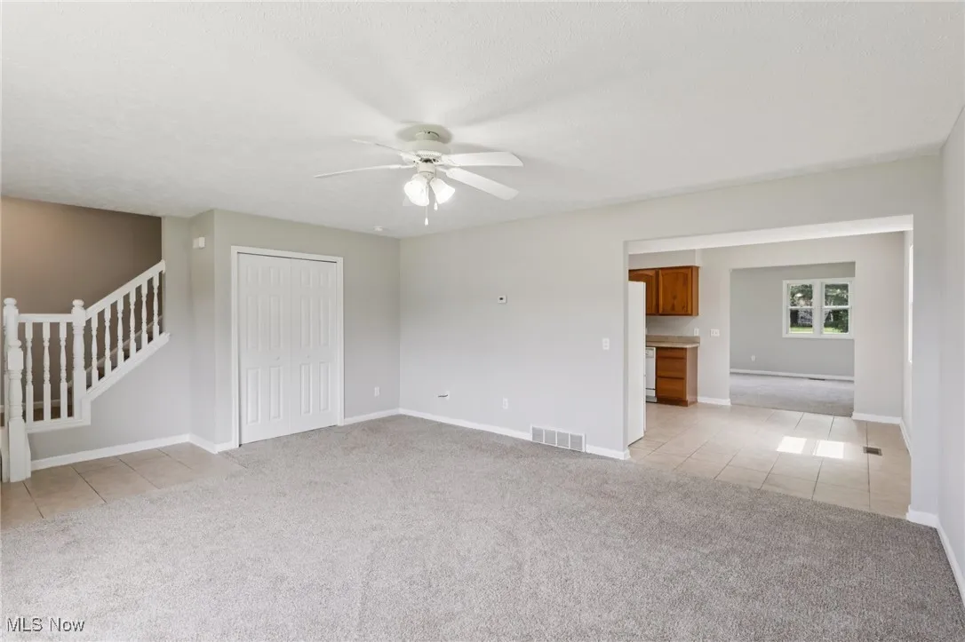 Unfurnished living room featuring light tile patterned floors, light colored carpet, a ceiling fan, and stairway