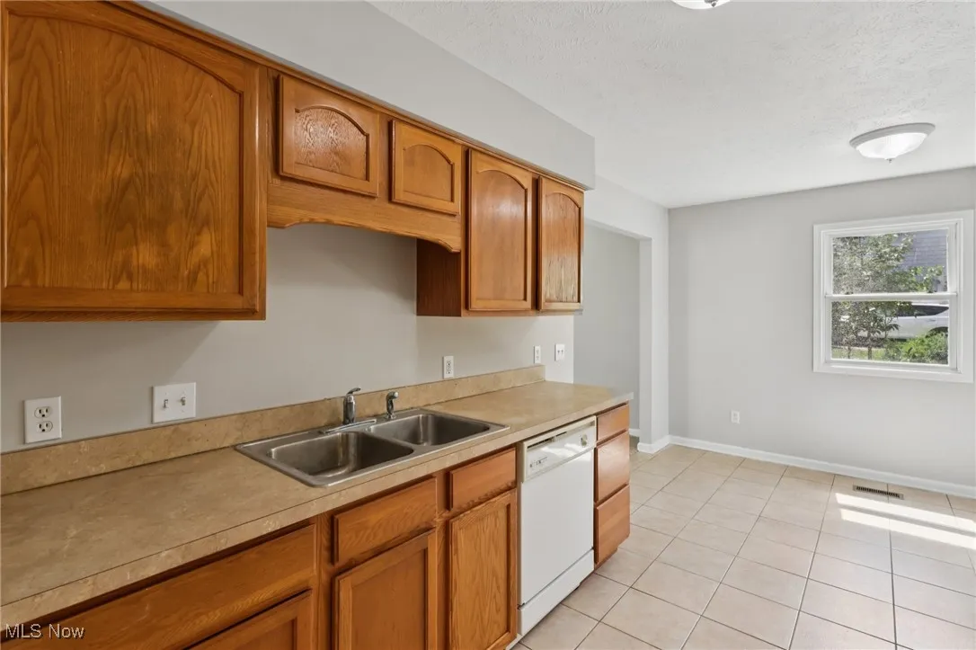 Kitchen with light tile patterned flooring, dishwasher, brown cabinets, light countertops, and a textured ceiling
