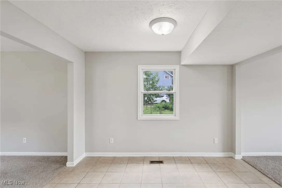 Unfurnished room featuring a textured ceiling, light carpet, and light tile patterned flooring