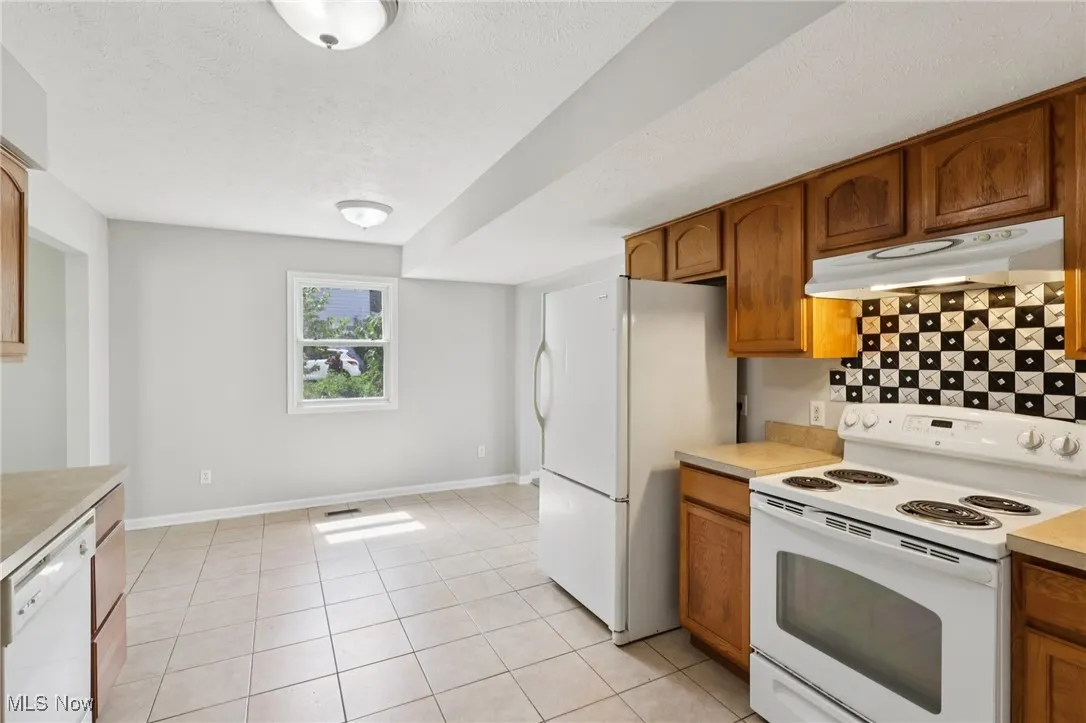 Kitchen with white appliances, under cabinet range hood, light countertops, light tile patterned floors, and a textured ceiling