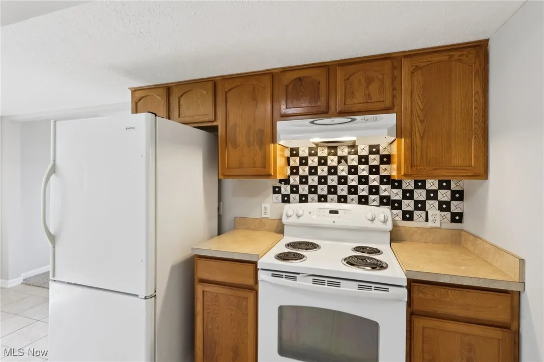Kitchen with white appliances, light countertops, tasteful backsplash, and brown cabinets
