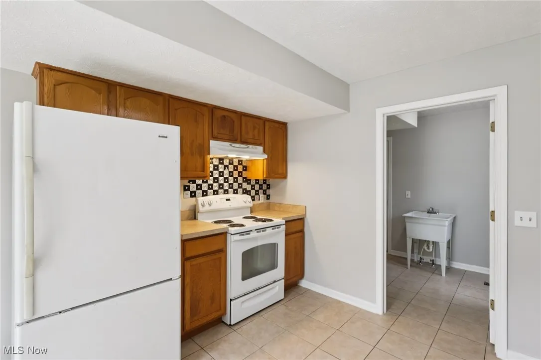 Kitchen with white appliances, brown cabinetry, light countertops, tasteful backsplash, and light tile patterned floors