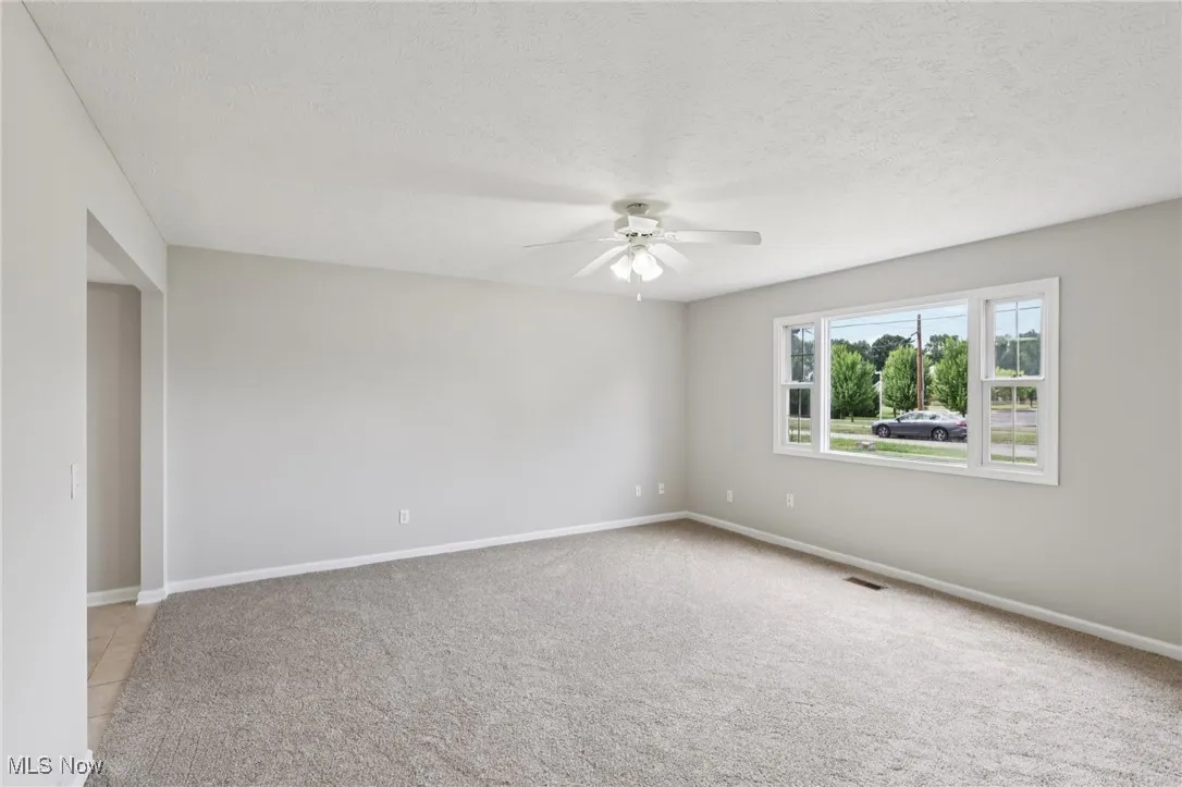 Unfurnished room featuring light colored carpet, ceiling fan, and a textured ceiling