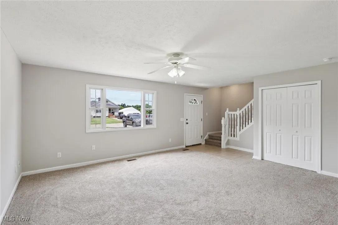 Unfurnished living room featuring stairway, light carpet, a ceiling fan, and a textured ceiling