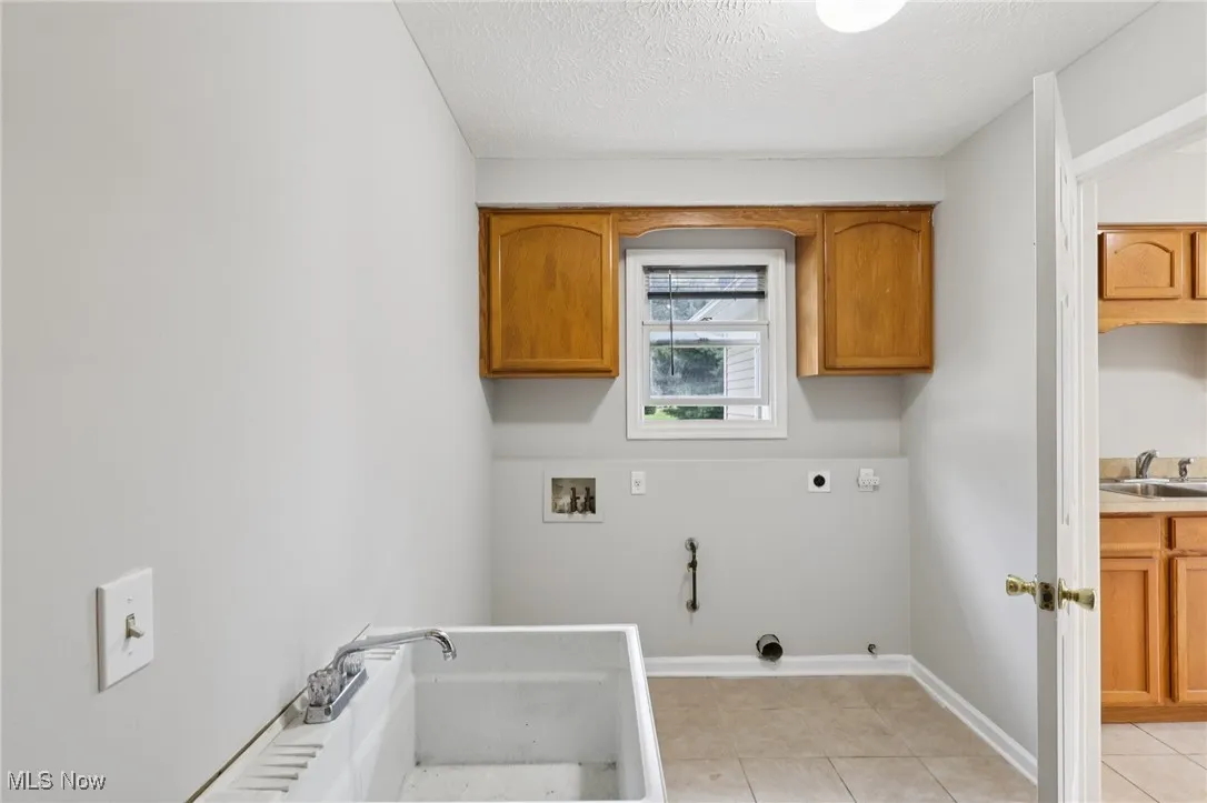 Laundry area with light tile patterned floors, a textured ceiling, hookup for a washing machine, gas dryer hookup, and hookup for an electric dryer