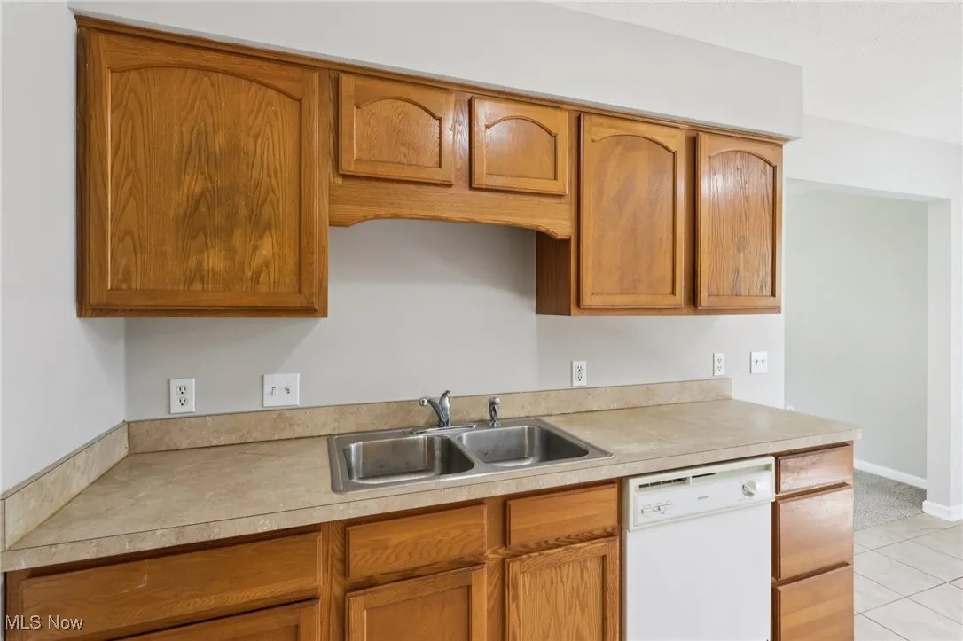 Kitchen featuring white dishwasher, light countertops, brown cabinetry, and light tile patterned floors
