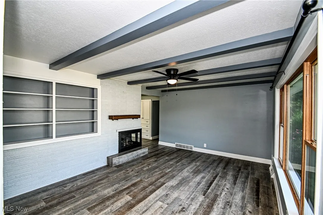 Unfurnished living room featuring a textured ceiling, dark wood-style floors, a ceiling fan, a large fireplace, and beamed ceiling