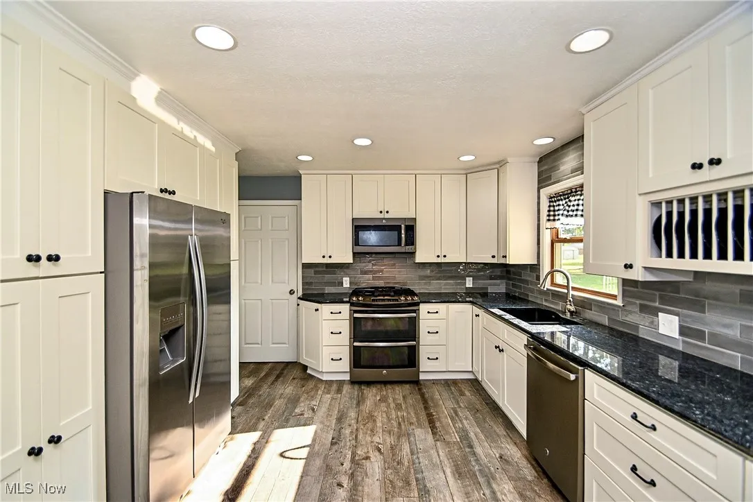 Kitchen with stainless steel appliances, dark wood-type flooring, tasteful backsplash, dark stone counters, and recessed lighting