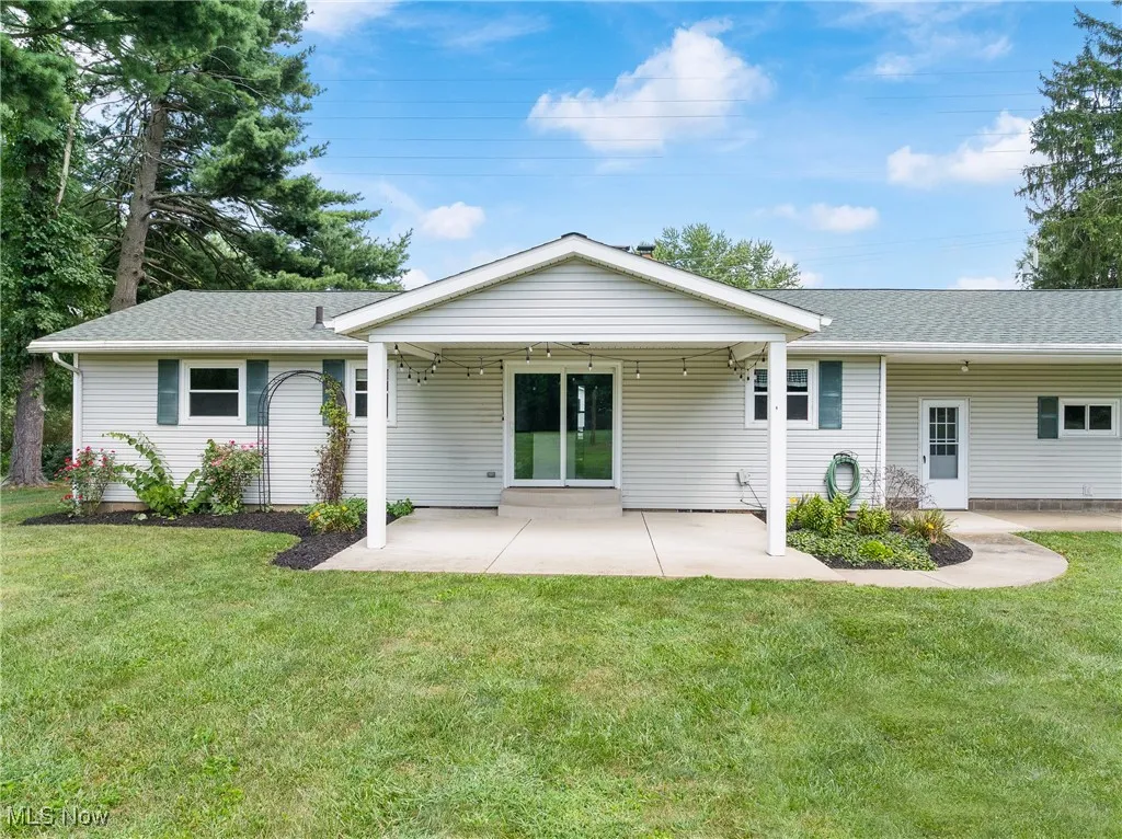 Back of house with a shingled roof, a lawn, and a patio
