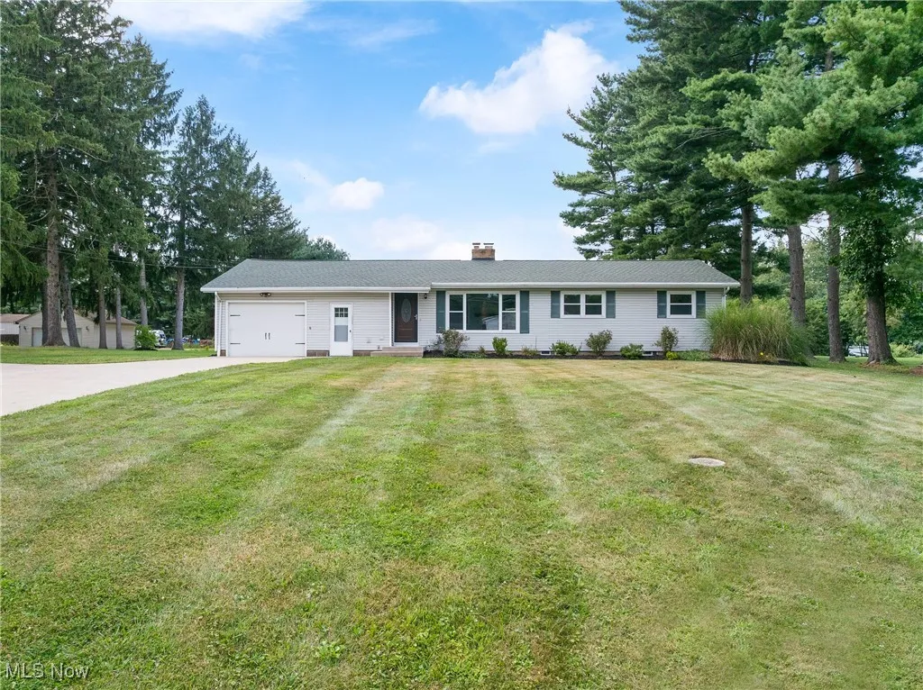 Ranch-style home featuring driveway, an attached garage, a front lawn, and a chimney