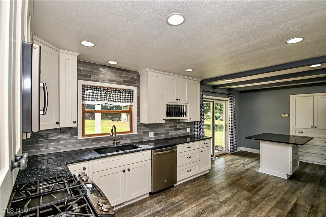 Kitchen featuring backsplash, white cabinets, stainless steel appliances, dark wood-type flooring, and a textured ceiling